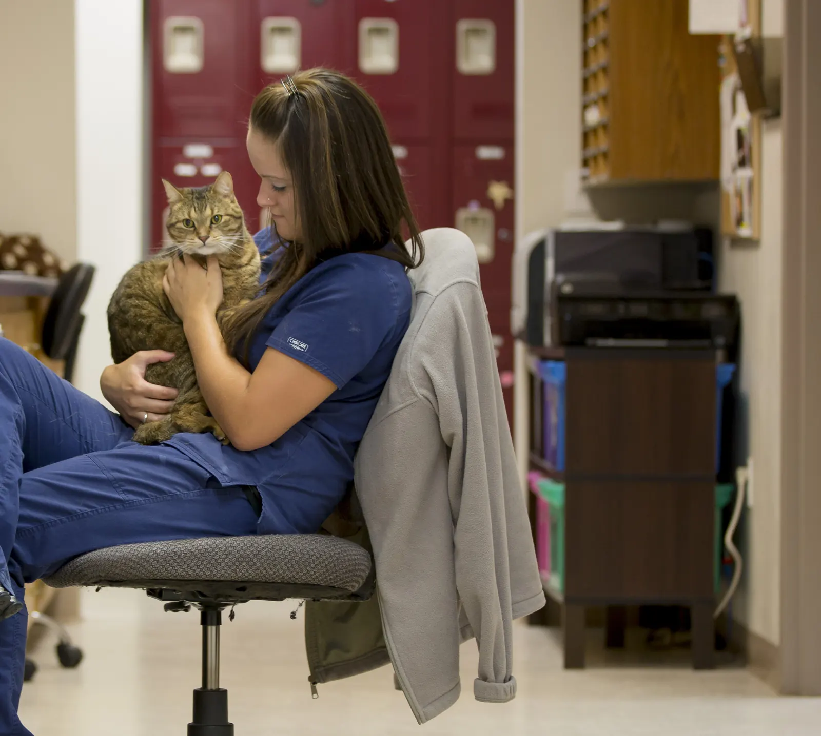 A Countrycare technician sits in the treatment area with a tabby cat cuddled on her lap