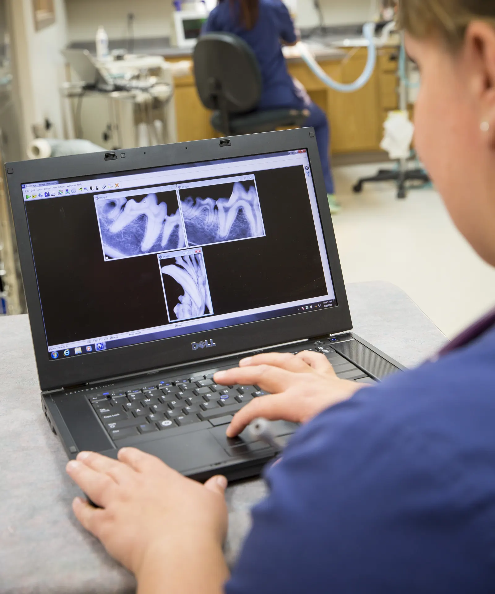 A Countrycare technician reviews dental x-rays on a laptop, the dental suite behind her