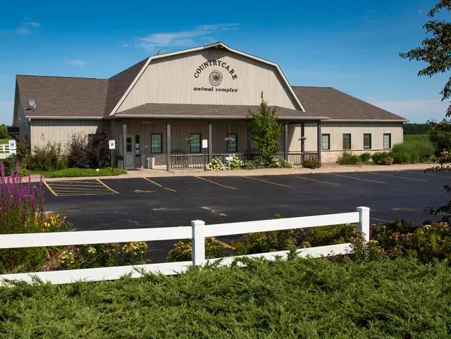 The Countrycare Animal Complex building, a tan barn-style clinic with its name on the gable, behind a white rail fence and flower beds.